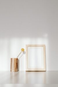 Elegant display of a wooden frame and vase on a white wall in natural light.